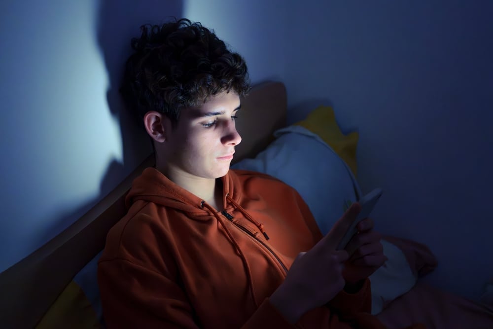 teenage boy scrolling through his phone at night
