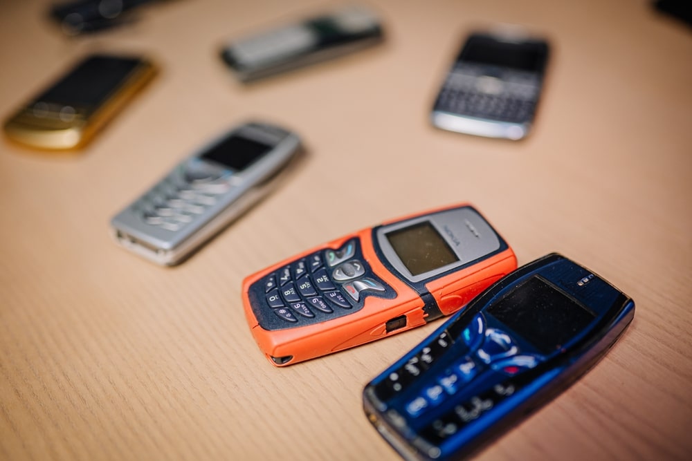 Collection of vintage mobile phones arranged on wooden table highlighting unique designs and colors for nostalgic appeal.