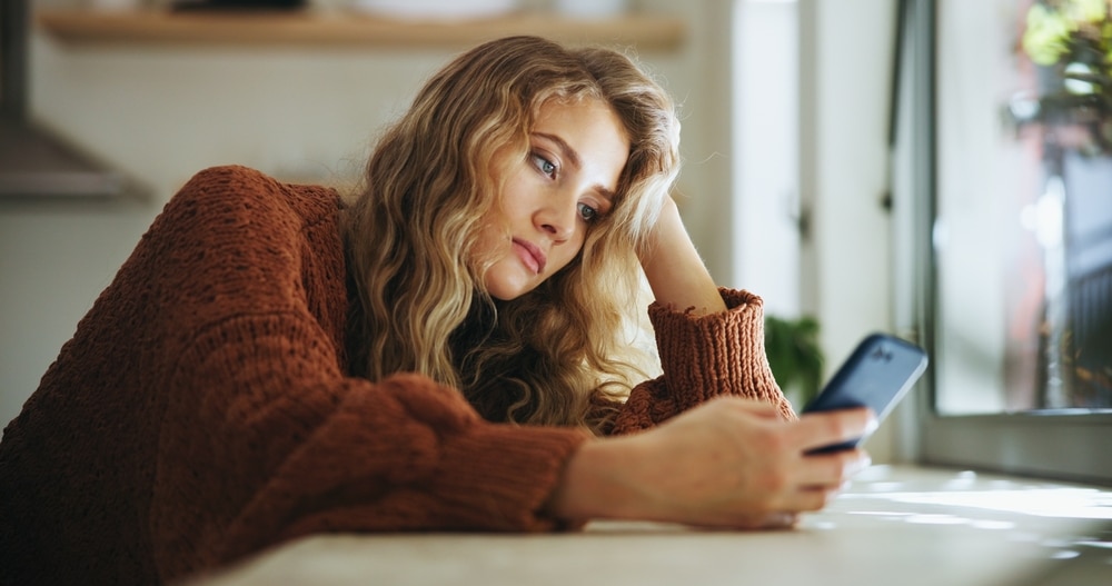 A woman stares dejectedly at her phone screen.