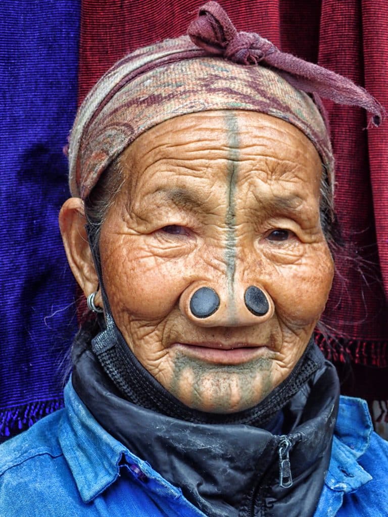 Image of an elderly Indian woman with traditional facial tattoos and two large nose plugs.