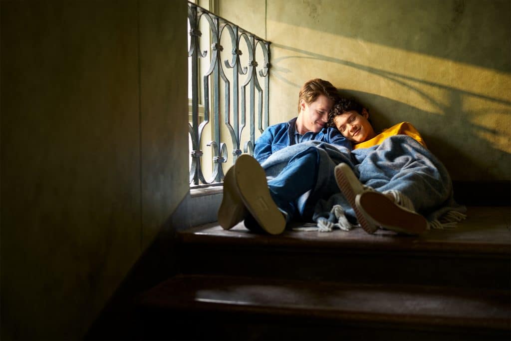 Wilhelm and Simon cozy up under a blanket next to each other on the stairs.