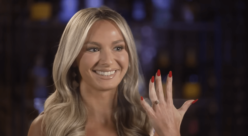 A woman holds up her hand to reveal an engagement ring.
