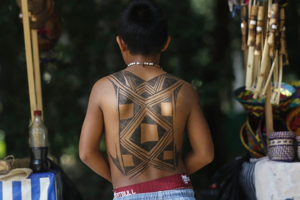 Image of a young Brazilian boy with a traditional geometric tattoo covering the majority of his back. He is facing away from the camera.