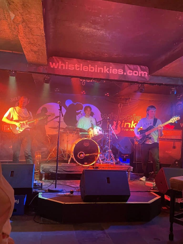 A trio band performing a song at Whistle Binkies Live Music Bar in Edinburgh, Scotland.