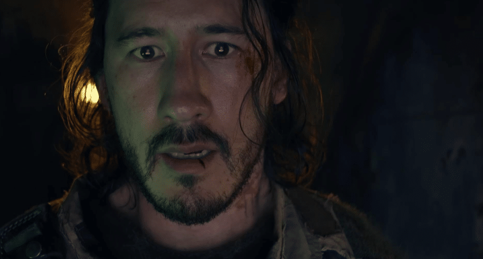 Candid image of the movie's protagonist, Simon. He appears distressed, against a dark back-drop, and has a cut on his lower lip, and a bloody scrape by his left eye.