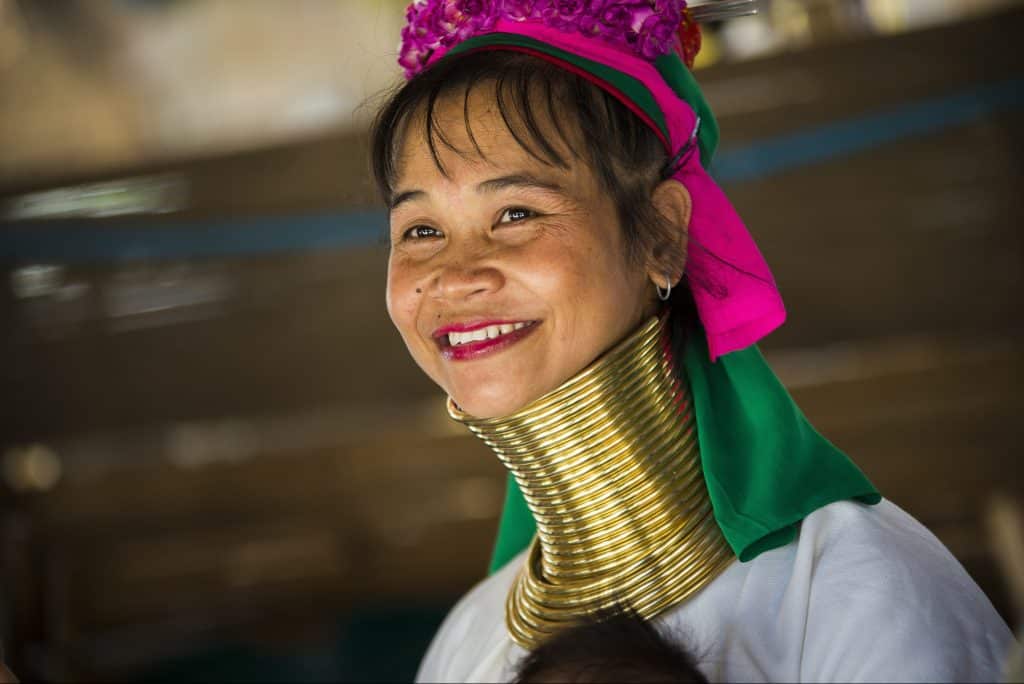 Image of a smiling Myanmar woman with a stretched neck wrapped in shiny brass rings.