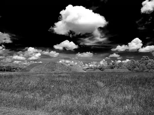 Black and white photograph of a field with a high contrast between fully formed clouds and a dark sky.