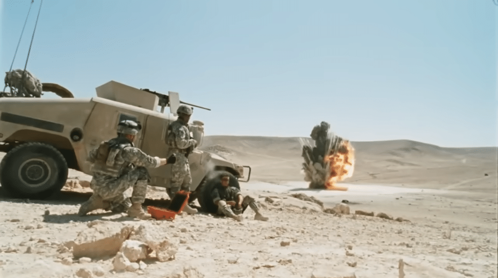 Three soldiers look on as massive controlled explosion takes place in a sandy desert.