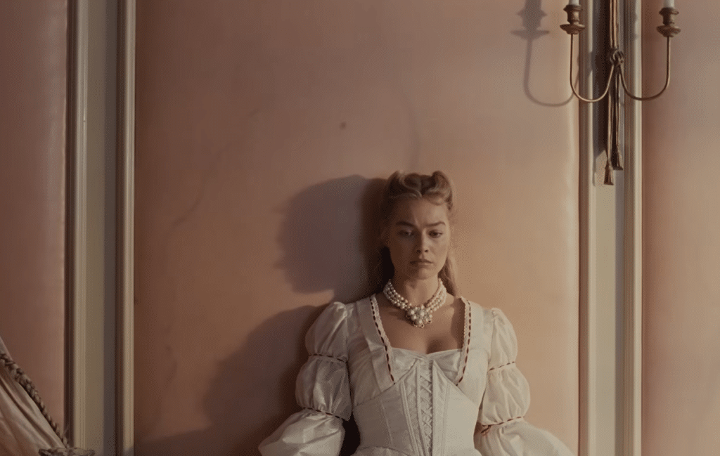 Margot Robbie as Catherine leans against the flesh-like wallpaper of her bedroom.