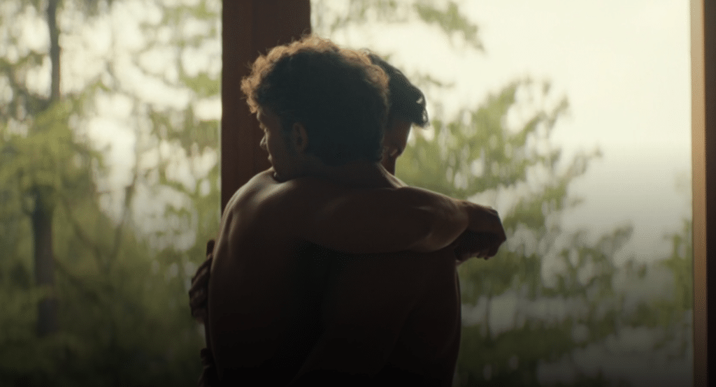 Ilya and Shane from Heated Rivalry, share in shirtless embrace in front of a window.