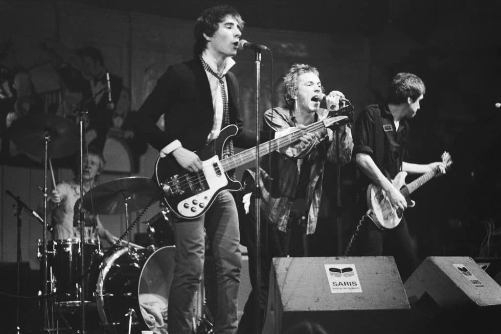 The Sex Pistols perform in Paradiso, Amsterdam. Lead guitarist Steve Jones (left) strums with Glen Matlock (right) and John Rotten (center) sings. Paul Cook plays drums in the back.