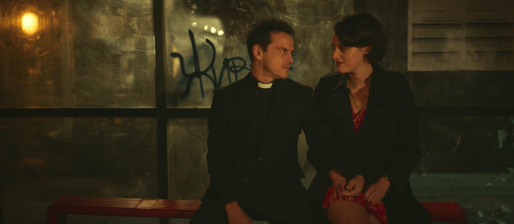 The Hot Priest and Fleabag sit next to each other with their hands interlocked at a bus station.