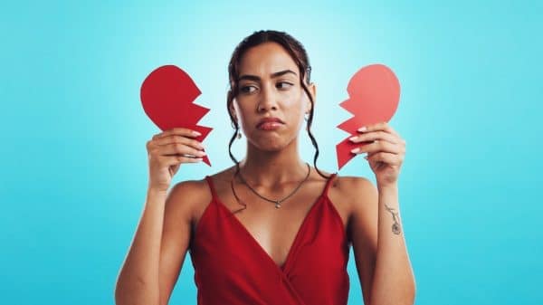 Sad woman holds a paper broken heart in her hands.