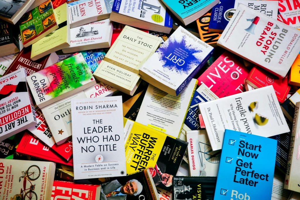 Overhead shot of various colorful books scattered on top of each other. The pile of books contain various titles on the topic of self-help.