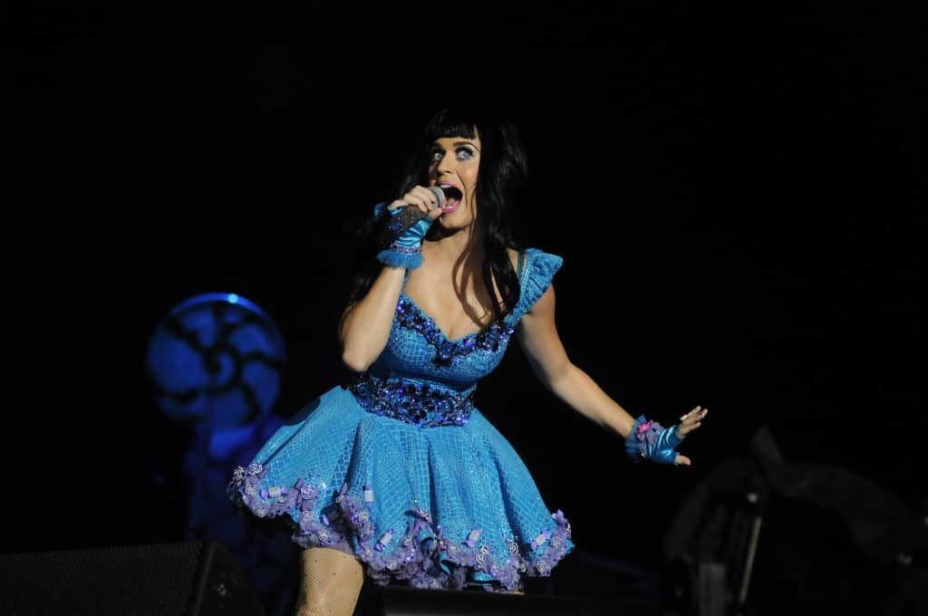 Katy Perry singing to crowd in a blue dress. Her mouth is wide open, and her hand spread outward to the left.