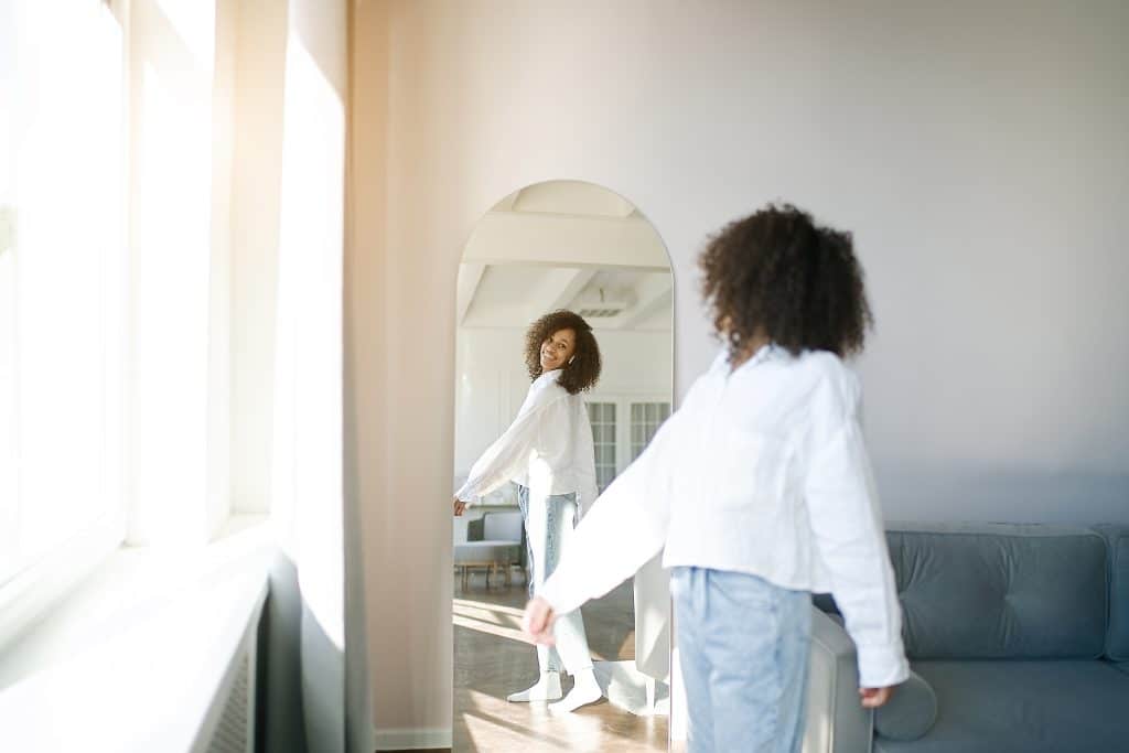 Image of a woman looking at herself in the mirror while smiling.