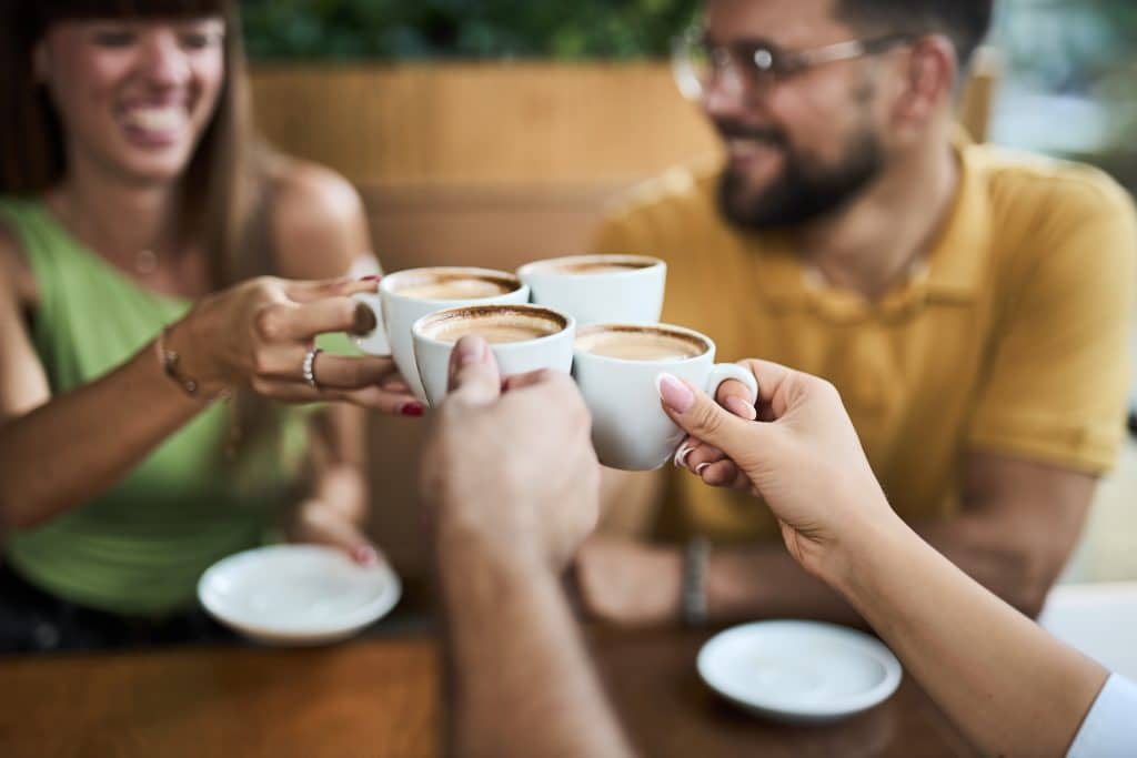 Four people clink filled coffee cups together.