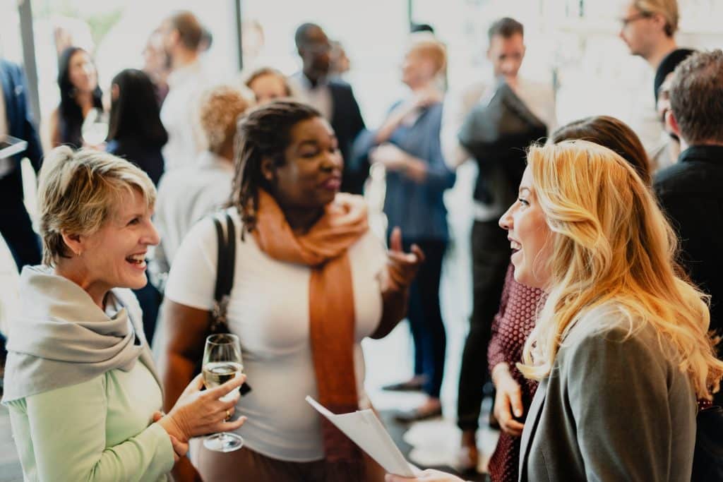 Four women converse with many people doing the same behind them at a mixer.