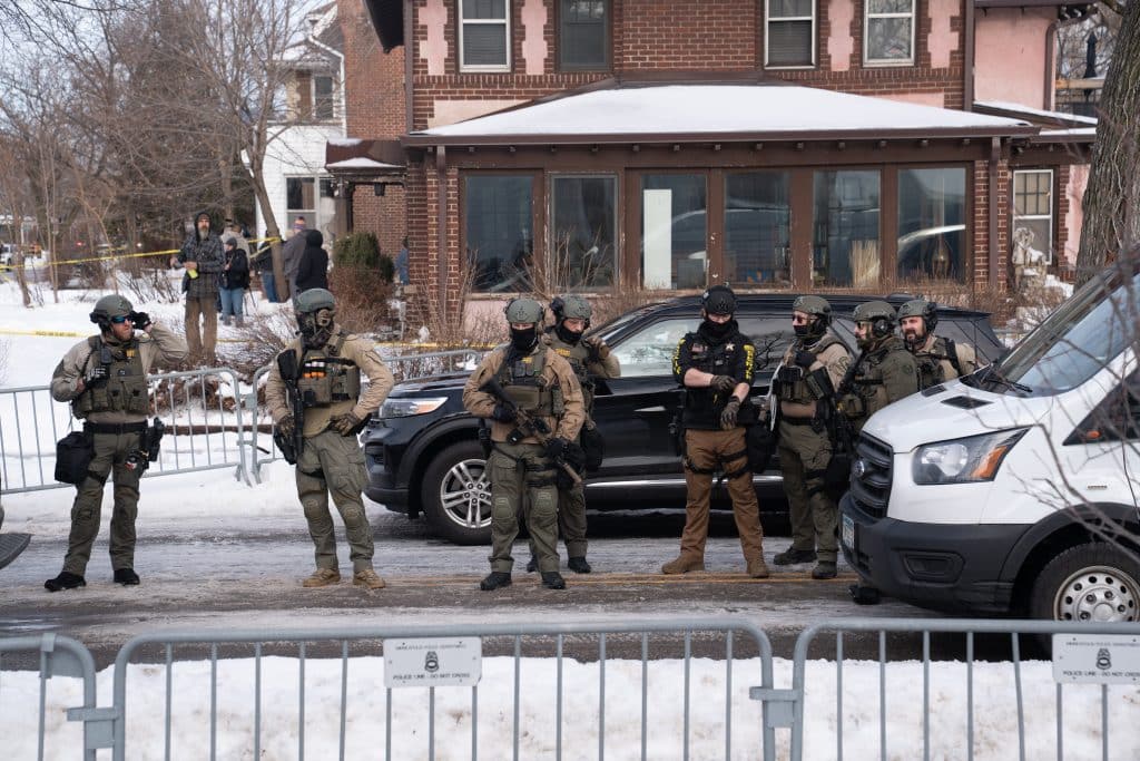 Law enforcement officers wearing tactical gear standing outside a residence.