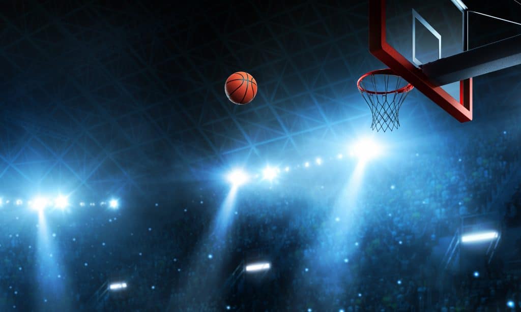 A basketball halfway to a net, glowing lights in the background.