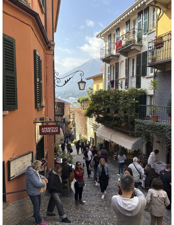 Picture of the stone streets in Bellagio. Features people walking, bars, restaurants, and shops.