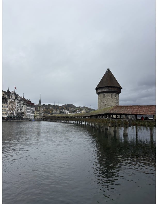 Picture of the water and the Chapel bridge in Lucurne. Far in the background there are mountains and other buildings, probably restaurants/shops.
