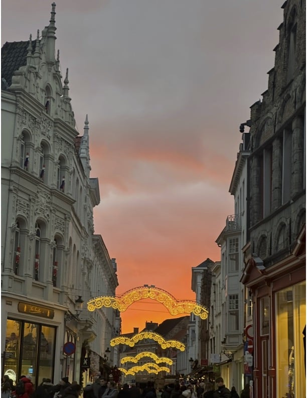 Sunset picture in Bruges, the sunset is orange with shades of pink. In the center of the image are lights used for decorating around Christmas time.