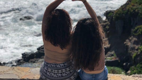 Two sisters sitting on a ledge making a heart shape with their hands above their heads.