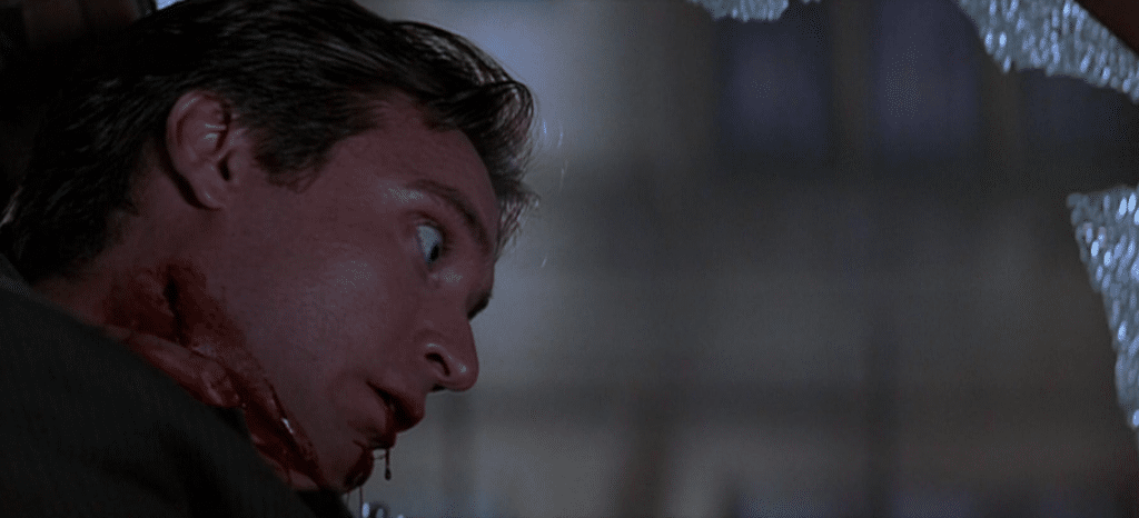 Screenshot from the second 'Scream' film of a man with a bloody throat, whose mouth is dripping blood. His eyes are wide open, and he appears dead.