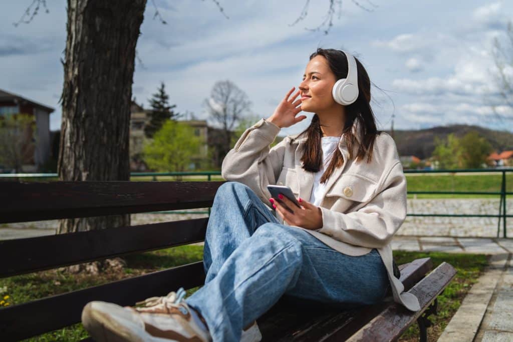 Girl sitting outside on bench hearing digital media