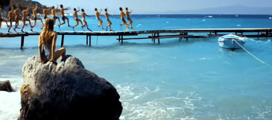 A girl sits on a rock whilst some men run along the pier