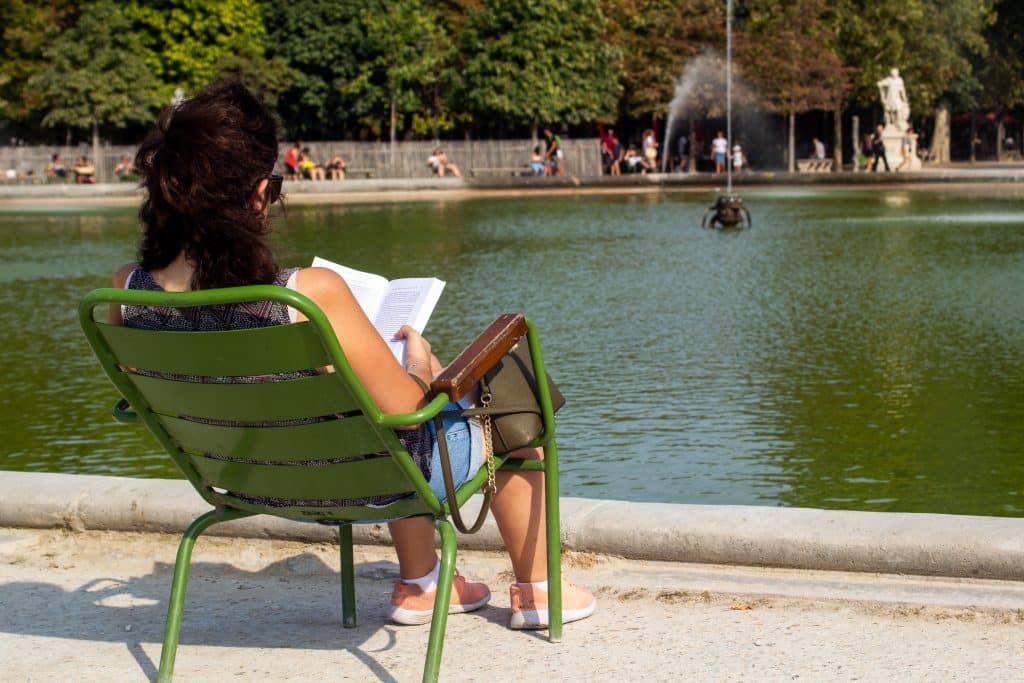 Girl reading in public near fountain.