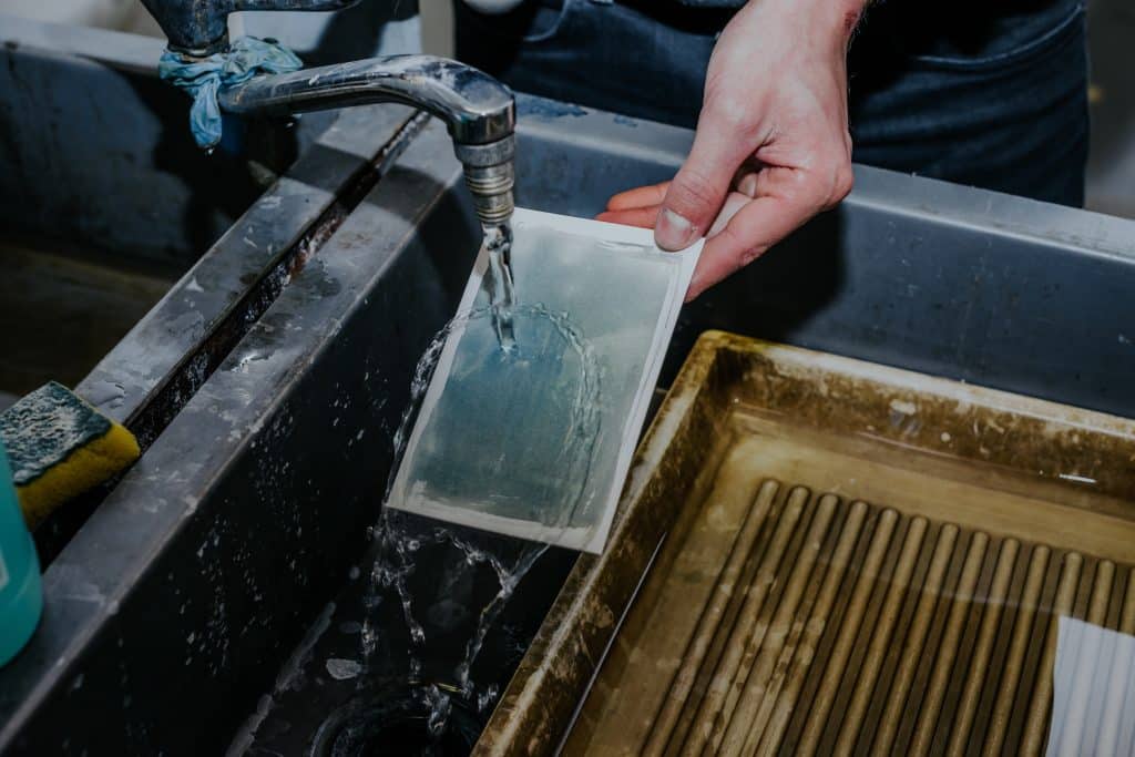 Photographer working in a lab creating custom cyanotype prints on craft paper. Chemicals, tools, and UV light exposure to develop unique, handcrafted blue-toned printmaking techniques