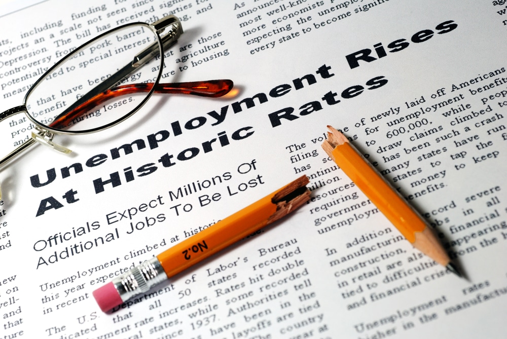 image of a newspaper with a story on the rise of unemployment, with a broken pencil and pair of glasses on it