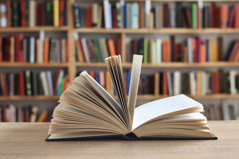 A single book flipped open and pages are all open with a blurred background of a bookshelf