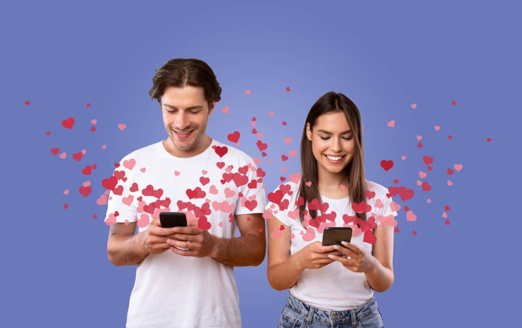 A man and woman smiling at their phones. Hearts emerge from their cellphone screens.