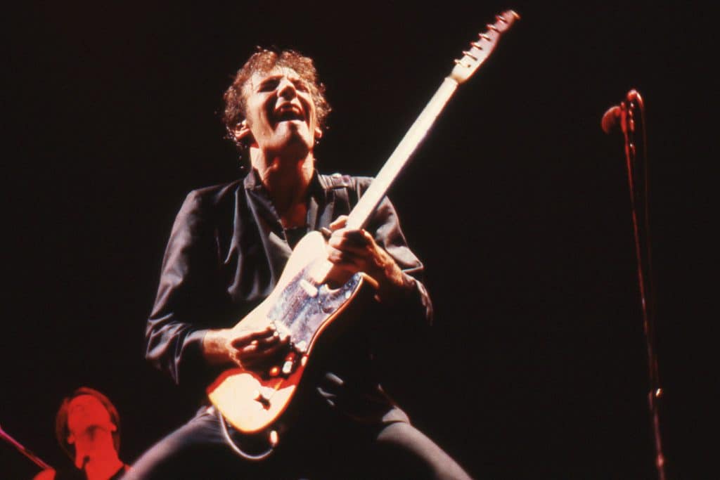 Bruce jamming on electric guitar under flashing lights during an energetic concert.