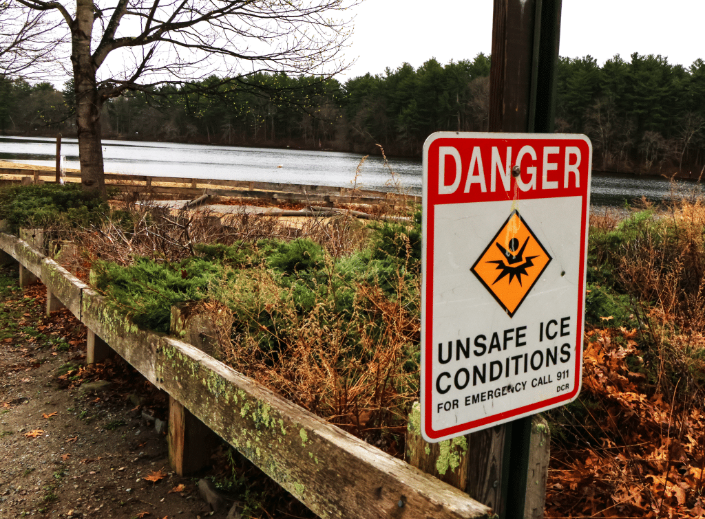 Full color photograph of a lake, greenery, and a sign that says "Danger, unsafe ice conditions"