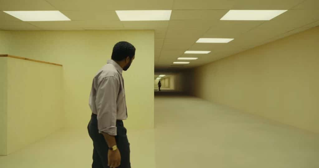 Photo of Chiwetel Ejiofor‘s unnamed character exploring The Backrooms. A dark figure stands at the end of the hall.