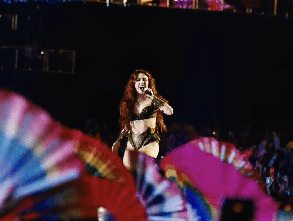 Chappell Roan performing to fans holding up LGBTQ+ flags.