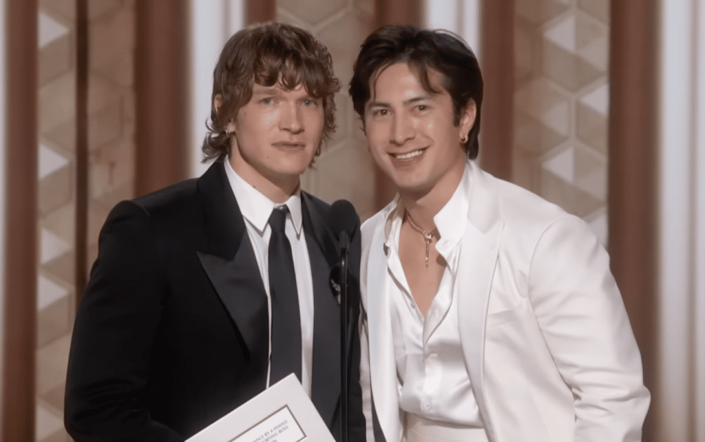 Connor Storrie (left) holds Golden Globe nomination envelope in black tux. Hudson Williams (right) smiles in white tux