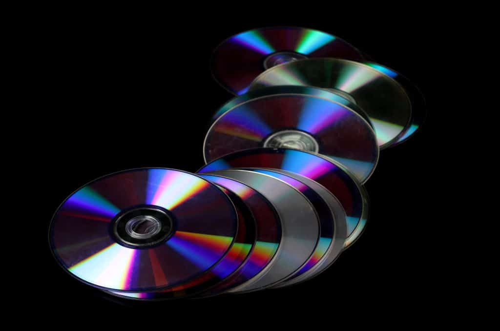 Movie discs laying in a line-like pile. Some of them reflect prismatic colors, others are just grey