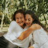 The image shows a mother and her adult daughter embracing outside.