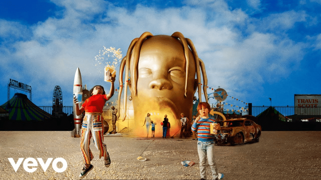 The official album cover for Travis Scott's Astroworld (2018) with a big golden inflatable of Scott's head serving as the entrance to an amusement park, with children, parents, and employees in front as well.