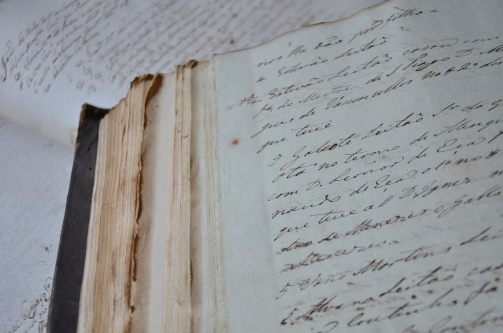 Close-up of an old, open book with frayed pages and handwritten, cursive text.