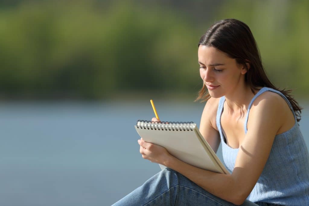 Woman sits in nature writing in a notepad.