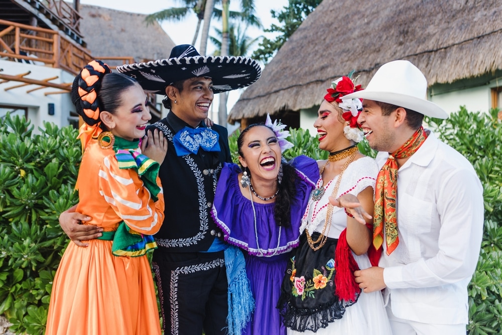 Mexican dancers in traditional costumes, laughing and smiling.