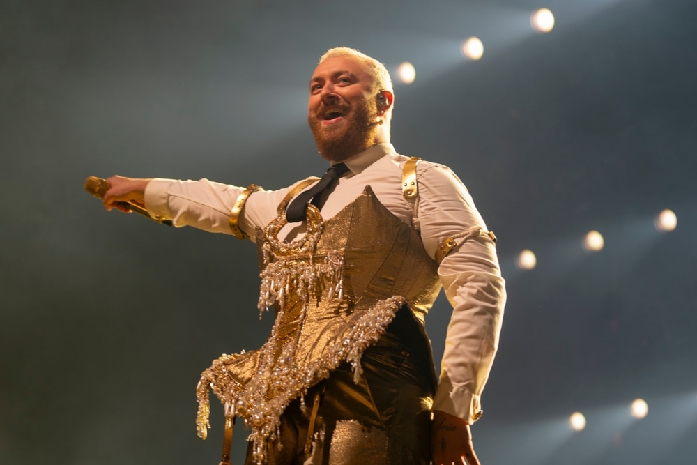 Sam Smith in bedazzled gold corset holding microphone in right hand