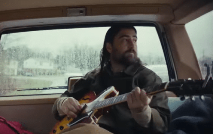 Noah Kahan playing guitar in "The Great Divide" music video.