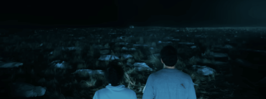 Couple standing in front of what looks like dead bodies at night